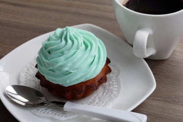 Cream cake and cup of coffee. Cake lies on a saucer. Near a coffee spoon.