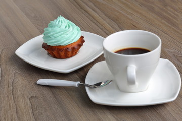 Cream cake and cup of coffee. Cake lies on a saucer. Near a coffee spoon.