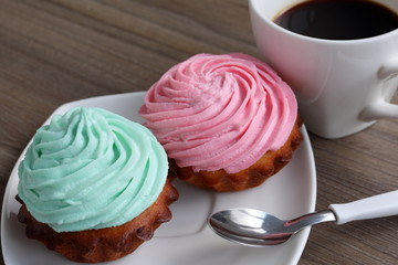 Two cream cakes and a cup of coffee. Cakes lie on a saucer. Near a coffee spoon.