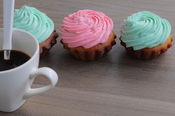 Three cream cakes of different colors and a cup of coffee. A coffee spoon is dropped into the coffee cup.