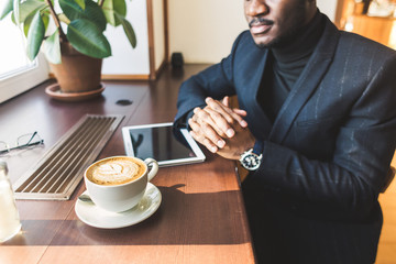 Fototapeta na wymiar Young handsome dark-skinned businessman with tablet in cafe with a cup of coffee.