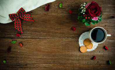 Coffee cup and biscuits on the wooden background in warm and cozy atmosphere. Decorated with red rose, ribbon and dried flowers. Copy space for design.