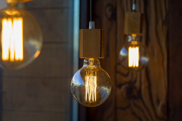 glowing spherical retro vintage edison incandescent bulbs against a blurred brown wall with a wooden texture and other lamps and blurred foreground