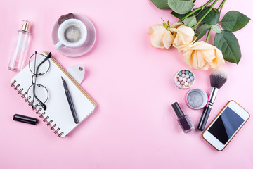 Workplace mockup with notebook, glasses, roses, phone and accessories on pink background top view. Flat lay with coffee copy space. Feminine working style concept.
