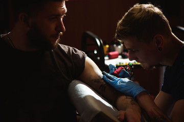 Professional tattoo artist makes a tattoo on a man's hand.