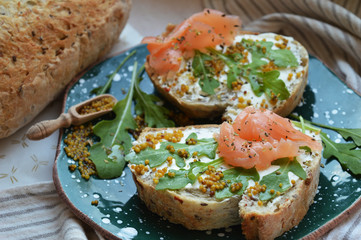 Homemade salmon sandwich with cream cheese, mustard seeds, olive oil, arugula on toasted rye bread, served on green ceramic plate. Healthy trendy food.