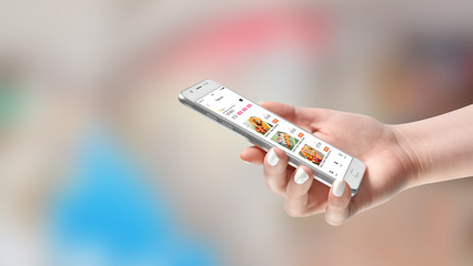 Female hand with food delivery app on her smartphone ordering meals, on blurred background