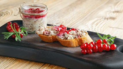 mackerel rillettes with berry confiture on baguette slices and a glass jar with rillettes on black serving board decorated with red currants and rosemary 