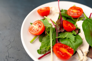 Mix fresh leaves of arugula, lettuce, spinach, tomato and chicken fillet for salad, on a white plate against a stone