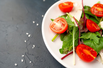 Mix fresh leaves of arugula, lettuce, spinach, tomato and chicken fillet for salad, on a white plate on a stone background with copy space for your text