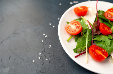 Mix fresh leaves of arugula, lettuce, spinach, tomato and chicken fillet for salad, on a white plate on a stone background with copy space for your text