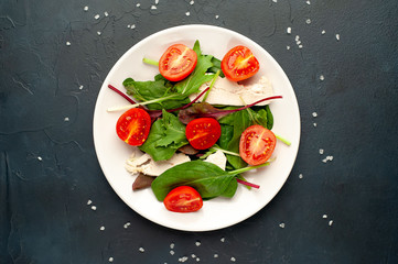 Mix fresh leaves of arugula, lettuce, spinach, tomato and chicken fillet for salad, on a white plate against a stone