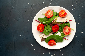 Fototapeta na wymiar Mix fresh leaves of arugula, lettuce, spinach, tomato and chicken fillet for salad, on a white plate on a stone background with copy space for your text