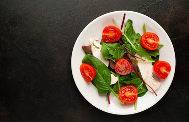 Mix fresh leaves of arugula, lettuce, spinach, tomato and chicken fillet for salad, on a white plate against a stone