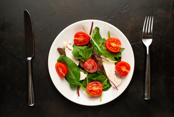 Mix fresh leaves of arugula, lettuce, spinach, tomato and chicken fillet for salad, on a white plate against a stone