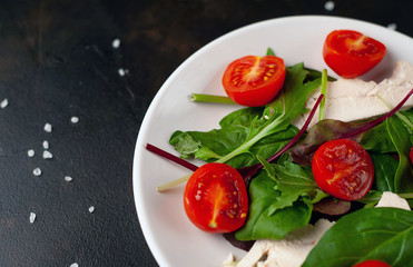 Mix fresh leaves of arugula, lettuce, spinach, tomato and chicken fillet for salad, on a white plate on a stone background with copy space for your text