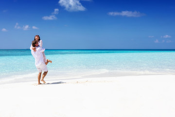 Fototapeta na wymiar Glückliches Liebespaar in weißen Sommerkleidern genießt den tropischen Strand auf den Malediven