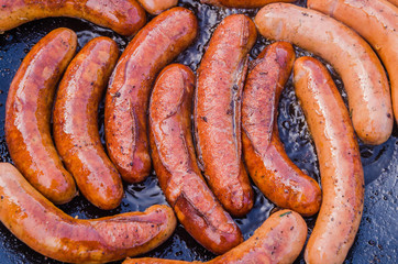 Street Food Market Vendor Cooking and Selling Sausages. Tasty Sausages on Large Commercial Griddle Hotplate. Street Food Cooking on Big Frying Pan Outdoor. Tongs In Hand Holding Sausages.