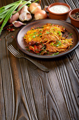 Homemade tasty potato pancakes in clay dish with sun-dried tomatoes and sour cream
