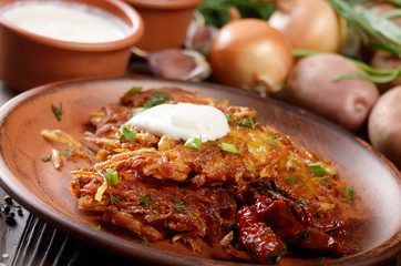 Closeup view at Homemade tasty potato pancakes in clay dish with sun-dried tomatoes and sour creram