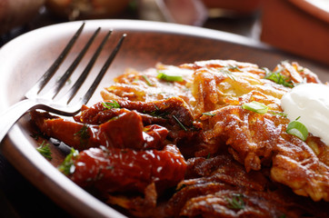 Closeup view at Homemade tasty potato pancakes in clay dish with sun-dried tomatoes and sour creram
