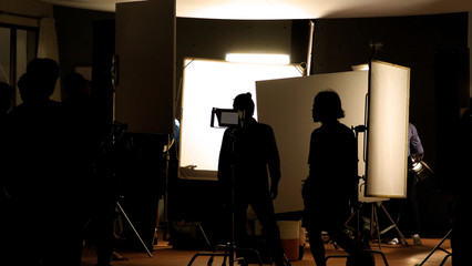 Fototapeta na wymiar Shooting studio behind the scenes in silhouette images which film crew team working for filming movie or video with professional lighting and equipment such as camera, tripod, soft box, monitor