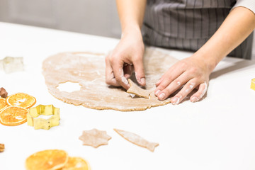 Young pretty woman prepares the dough and bakes gingerbread and cookies in the kitchen. She makes a star shape on the dough. Merry Christmas and Happy New Year.