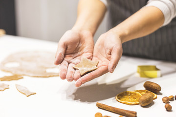 Young pretty woman prepares the dough and bakes gingerbread and cookies in the kitchen. She holds a star cut from the dough in her hands. Merry Christmas and Happy New Year.