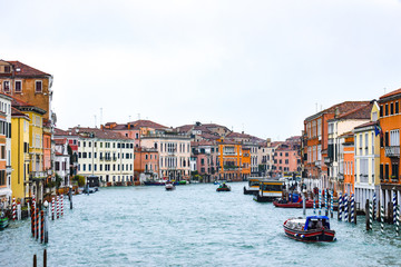 Water Taxis and other boats sailing between Venetian buildings along the Grand Canal in Venice, Italy. Striped poles on either side of the river are to help water vessels when navigating and mooring.