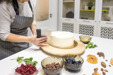 Confectioner smooths white cream on a biscuit cake with a cooking spatula. The concept of homemade pastry, cooking cakes.