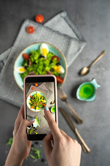 Hands of the girl with the phone close-up photography food. Green salad on the background of a concrete table in the style of lifestyle. Proper nutrition and food blogging.