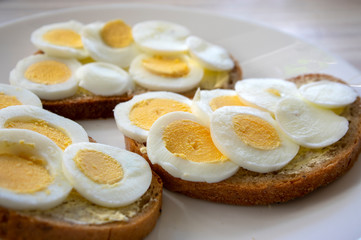 Sliced hard boiled eggs on common czech bread with butter on white plate on light wooden table