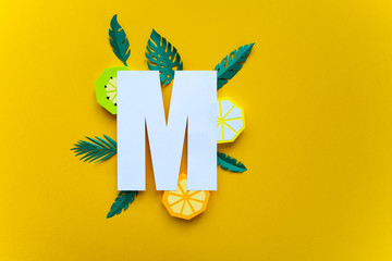 letter m cut from paper with tropical fruit paper
