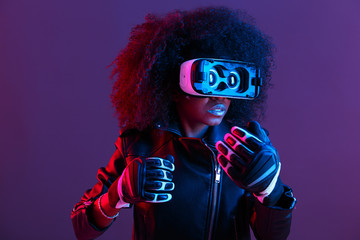 Curly dark haired girl dressed in black leather jacket and gloves uses the virtual reality glasses...