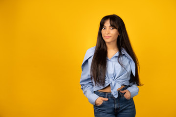 Young beautiful girl in a blue shirt posing for a photo on a yellow background.