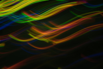 Blurry horizontal wavy lines. Multicolor neon lights in motion on dark background. Bokeh lens flare glow.