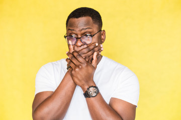 Surprised handsome African American man in glasses covers mouth in shock.