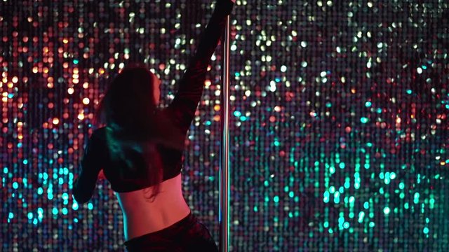 Alluring woman with long hair dancing with pylone on shining beautiful wall background. Sexy moving. Art, dance, sport concept