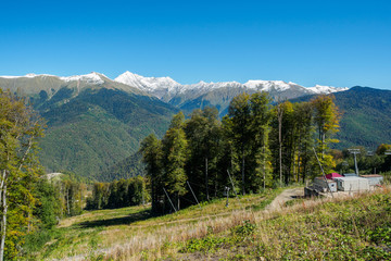 Green slopes of mountains with snowy peaks and cable cars