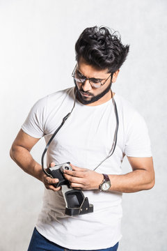 Portrait of a handsome young stylish man with beard taking photo on a vintage camera.