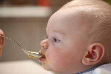 A child of 6 months pedagogical feeding from a spoon of porridge.