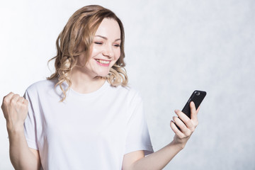 Happy young woman holding smartphone and celebrating his success.