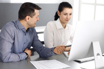 Obraz premium Cheerful smiling businessman and woman working with computer in modern office. Headshot at meeting or workplace. Teamwork, partnership and business concept 