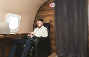 Young attractive and successful businessman is resting and listening to music works while sitting in the chair of his private business plane