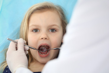 Little baby girl sitting at dental chair with open mouth and feeling fear during oral check up while doctor. Visiting dentist office. Medicine concept