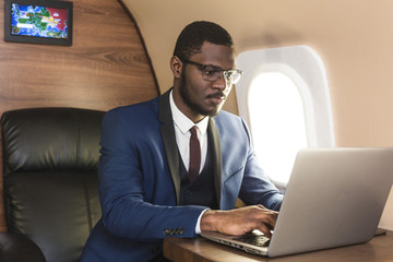 Attractive and successful African American businessman with glasses working on a laptop while...