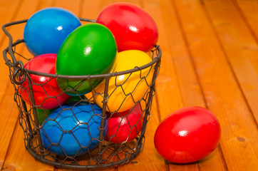 Decorated Easter eggs in wire basket on rustic wooden background