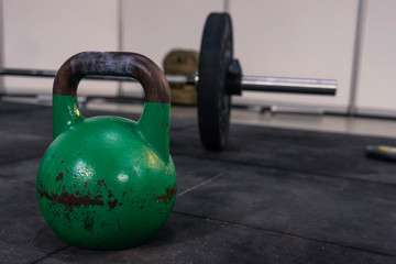 Naklejka na ściany i meble Kettlebell on a rubber mat, barbell ready for exercise in the background. Sporting equipment used in a cross training and cross fit physical exercise systems.