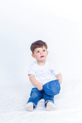 Cute baby in blue jeans, white t-shirt and denim baseball cap sits isolated on white background