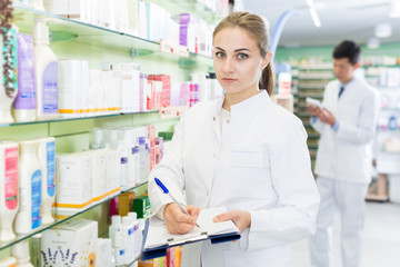 Female pharmacist is attentively looking medicine with notebook
